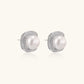 Rhodium-plated sterling silver stud earrings with round freshwater pearls surrounded by geometric crystal halos on cream background.