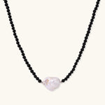 Beaded black agate necklace with iridescent baroque freshwater pearl centerpiece on cream background.