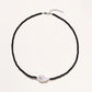 Beaded black agate necklace with iridescent baroque freshwater pearl centerpiece on cream background.