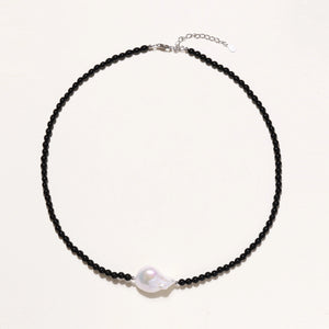 Beaded black agate necklace with iridescent baroque freshwater pearl centerpiece on cream background.