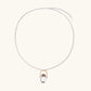 Whimsical owl pendant holding a white pearl on a gold swing, rhodium-plated silver chain on cream background.