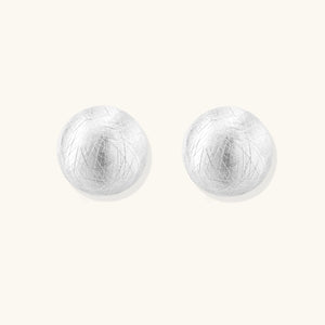 Brushed sterling silver half-dome clip-on earrings with textured surface against cream background