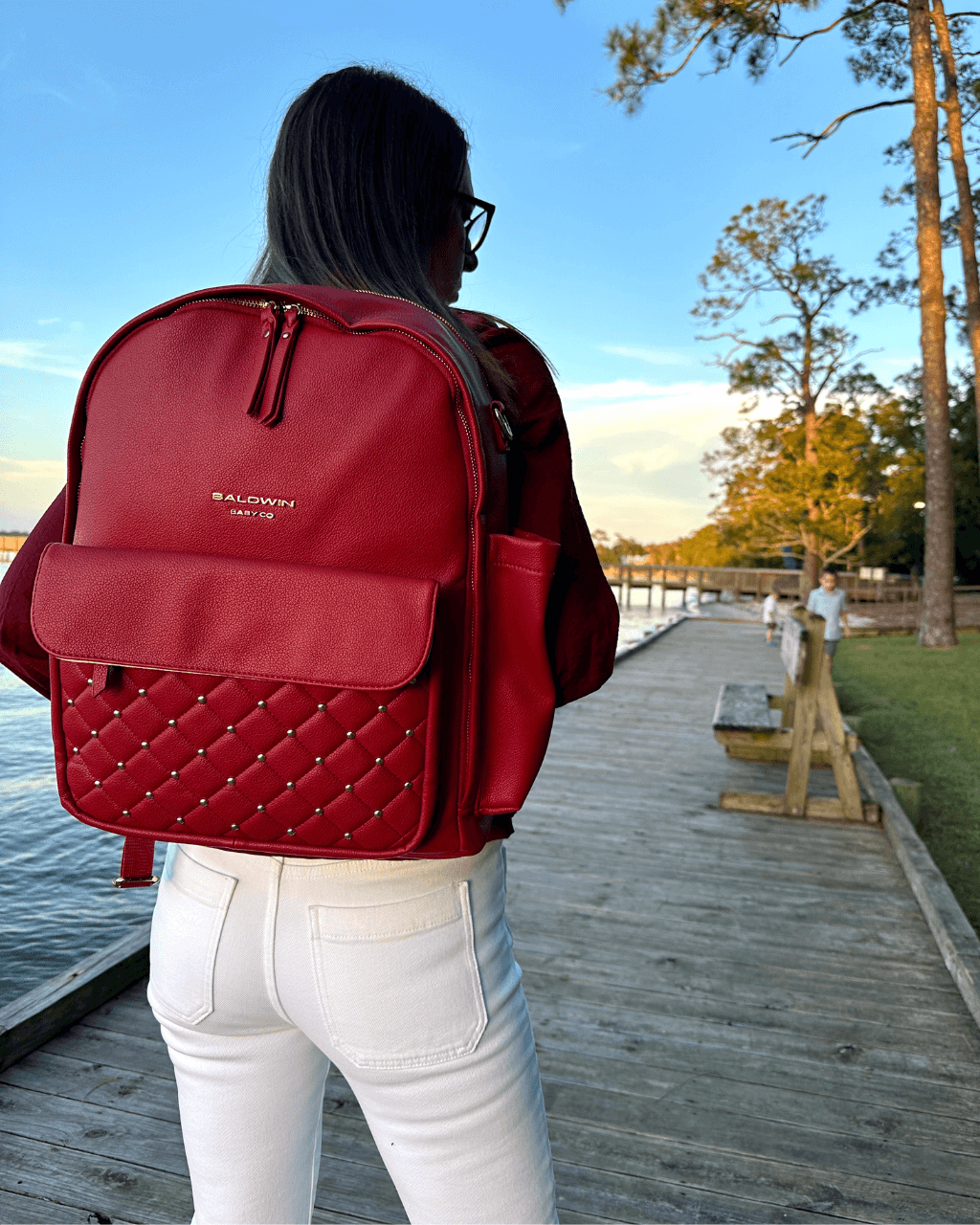 Baldwin Baby Company Daphne diaper bag in crimson, shown in a boardwalk lifestyle setting