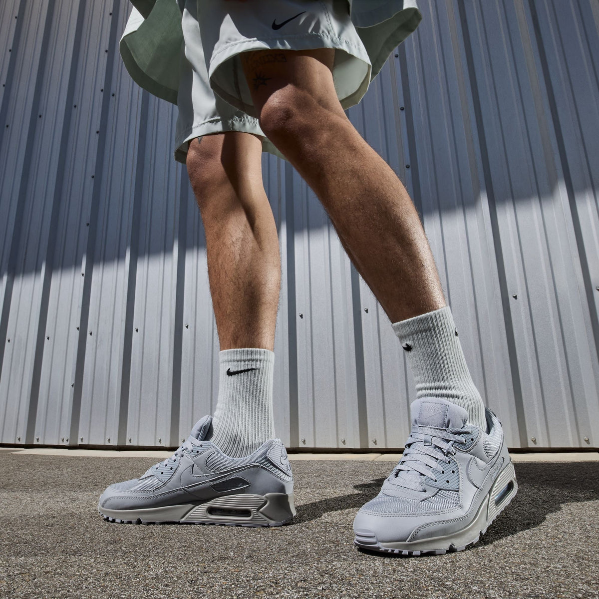 Nike men's Air Max 90 sneakers in Wolf Grey and black, side view.