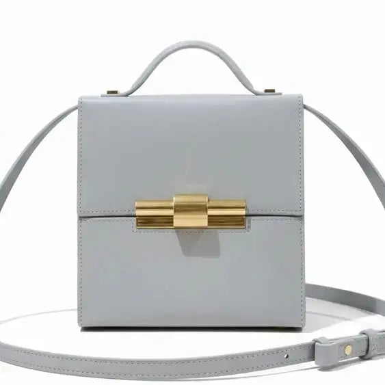 Thebagicon Nina cigar box bag in black leather with gold-tone hardware, featuring a structured rectangular shape and top handle.