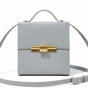 Thebagicon Nina cigar box bag in black leather with gold-tone hardware, featuring a structured rectangular shape and top handle.