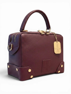Thebagicon Petite Grandmere Trunk Bag in leather, featuring a compact handbag design with a top handle and detailed stitching.
