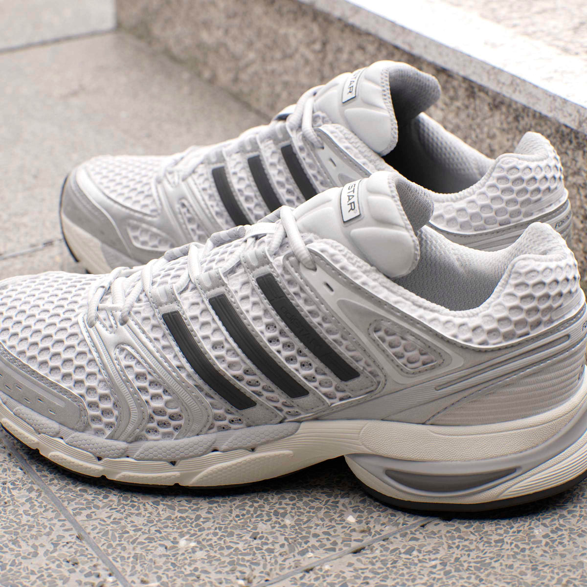 Silver Adidas men's Adistar Control 5 running shoes displayed on a plain background, showcasing the sleek design and branding.