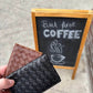 Deux Mains woven card holder in leather, shown with fall accessories in a coffee shop setting